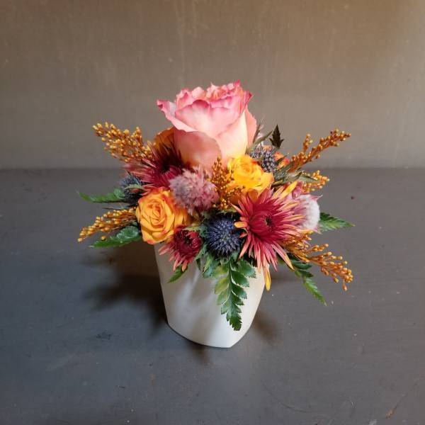 Pink rose arrangement in a white vase with yellow and red accent flowers