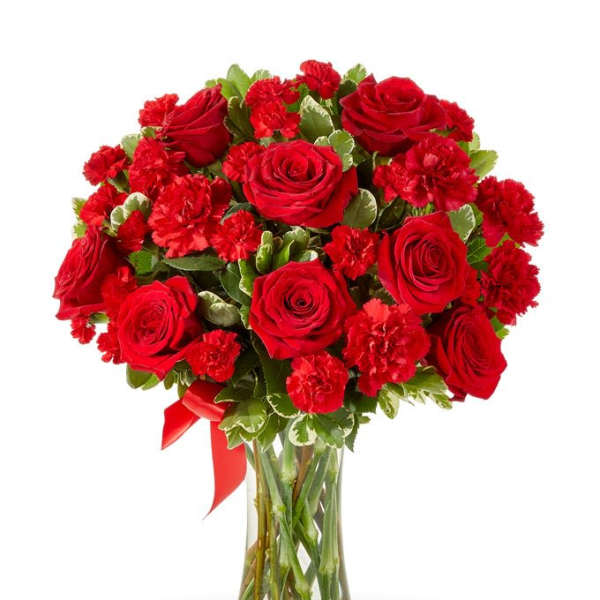 Red roses and carnations in a clear glass vase with a red ribbon