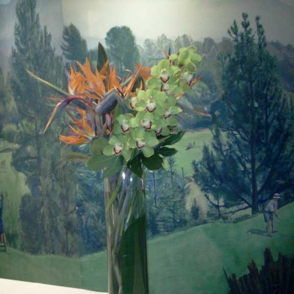 Tall vase arrangement with green orchids and orange tropical flowers