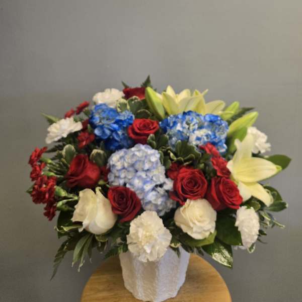Mixed bouquet of red roses, blue hydrangeas, white carnations, and pale lilies in a white vase