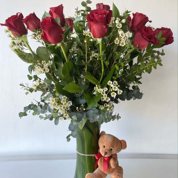 Red roses in a glass vase with a small teddy bear attached