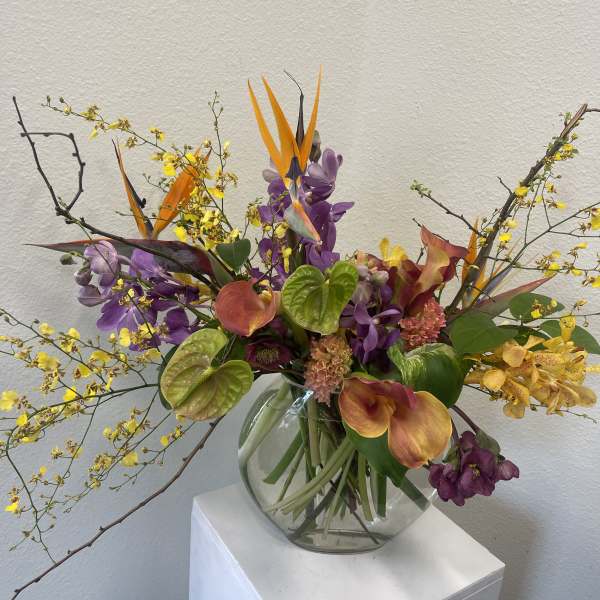 Mixed tropical bouquet in a clear glass vase with orange bird-of-paradise and purple orchids