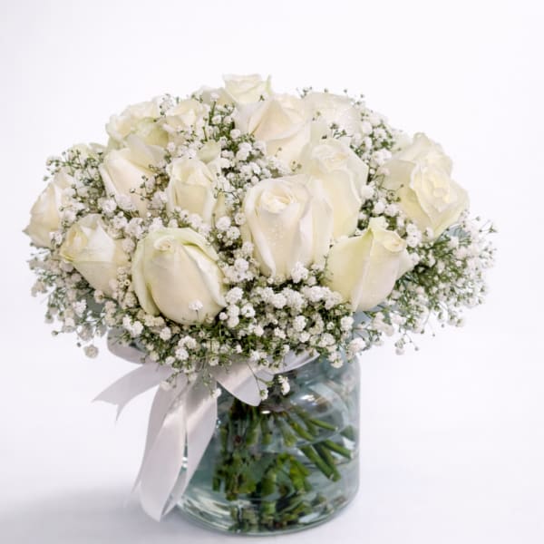 White rose bouquet in a glass vase with baby's breath and a ribbon