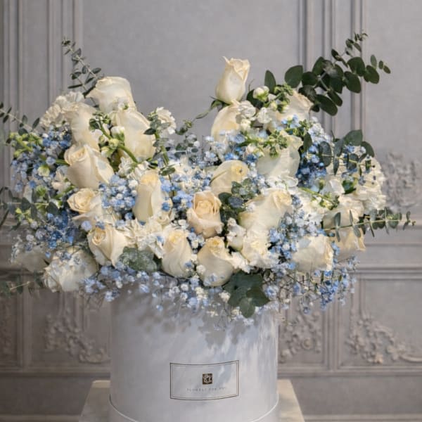 White roses and blue flowers arranged in a round hatbox