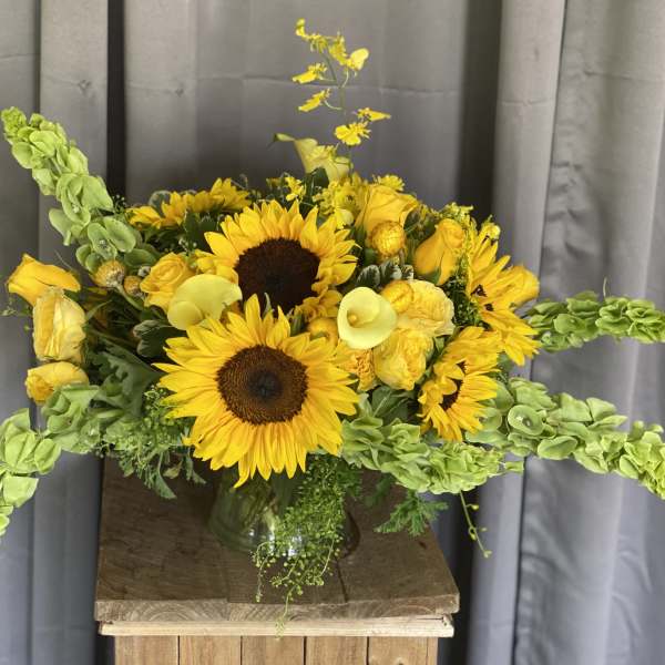 Yellow sunflower bouquet with roses and calla lilies in a glass vase