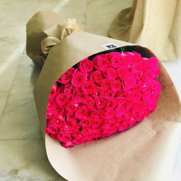 Large bouquet of bright pink roses wrapped in brown kraft paper and ribbon