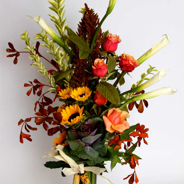 Tall mixed bouquet with roses, sunflowers, and white calla lilies in a glass vase