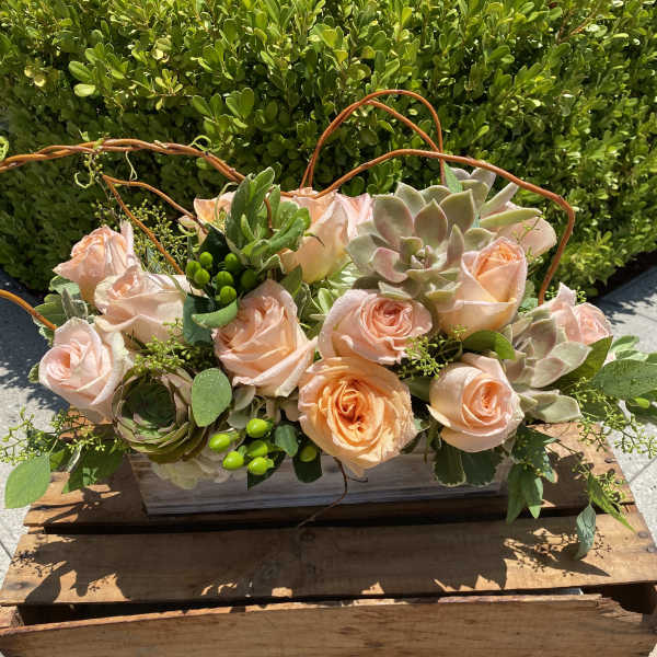 Peach roses and succulents arranged in a wooden box with curved twig handles