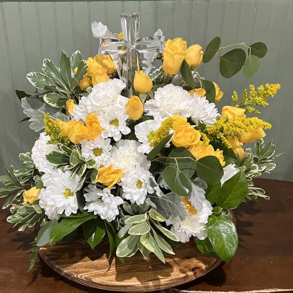 Yellow roses and white daisies arranged on a wooden tray with a silver cross