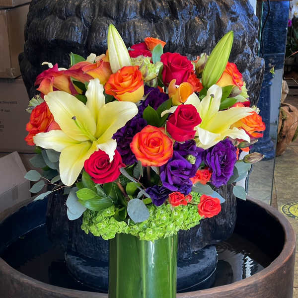 Bouquet of lilies, roses, and purple blooms in a tall green vase