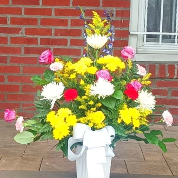 Colorful mixed flower arrangement in a white container with a ribbon