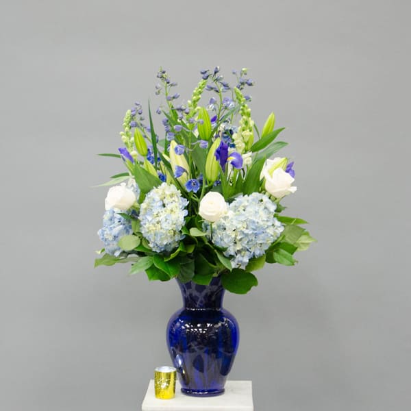 Blue and white floral arrangement in a cobalt vase with a small candle beside it.