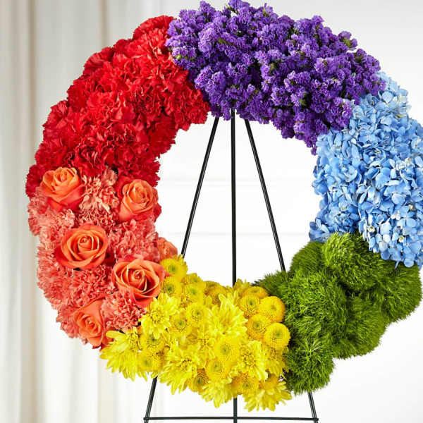 Rainbow floral wreath on a black stand with roses, carnations, hydrangeas, and mums