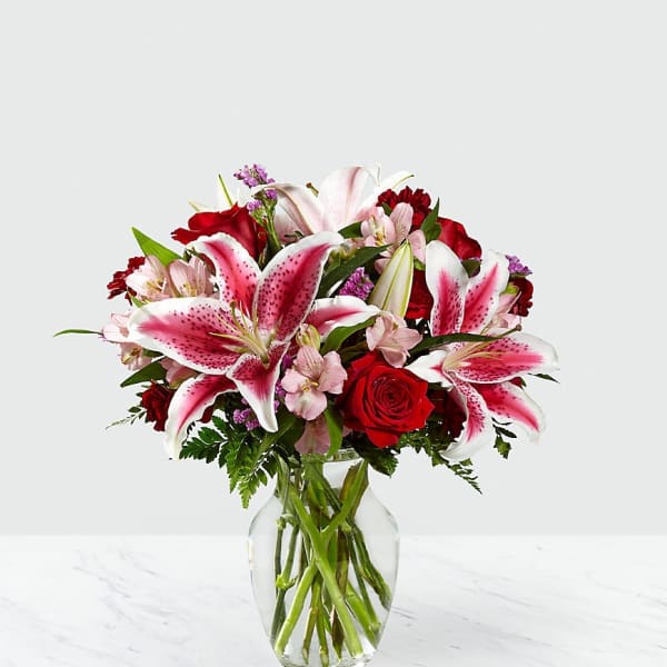 Bouquet of pink lilies and red roses in a clear glass vase