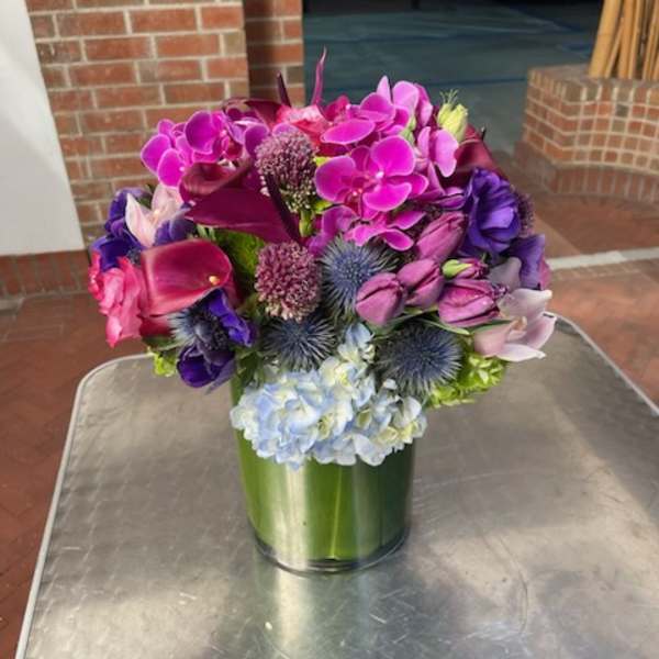 Colorful bouquet with orchids, calla lilies, hydrangea, and thistle in a green vase