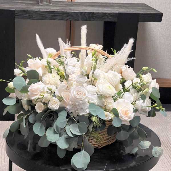 White rose arrangement in a wicker basket with eucalyptus and feathery accents