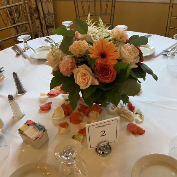 Round table centerpiece with peach and orange flowers in a low arrangement