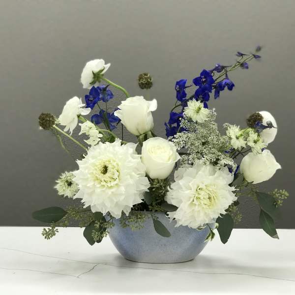 White and blue floral arrangement in a round blue vase
