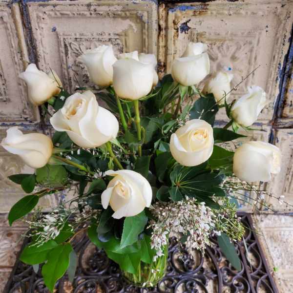 White roses arranged in a clear glass vase with greenery