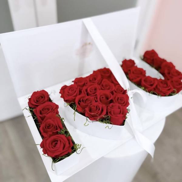 Red roses arranged in white gift boxes forming the letters I and U