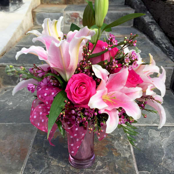 Pink lilies and roses arranged in a glass vase with a polka-dot ribbon.