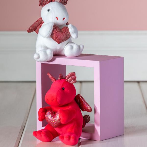 Two plush dragon toys holding glittery hearts on a pink block