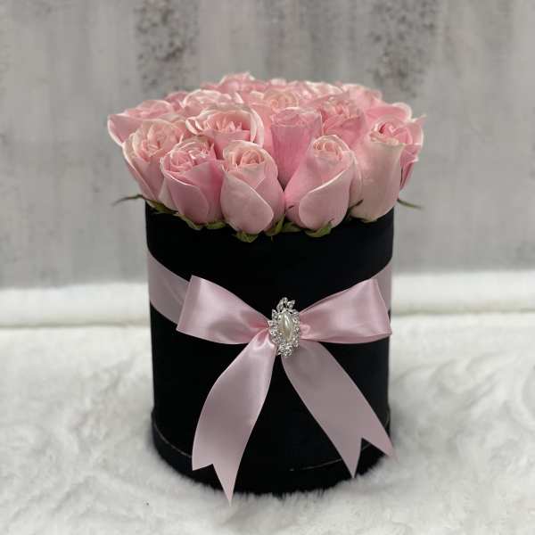 Round black hatbox filled with light pink roses and tied with a pink satin bow.