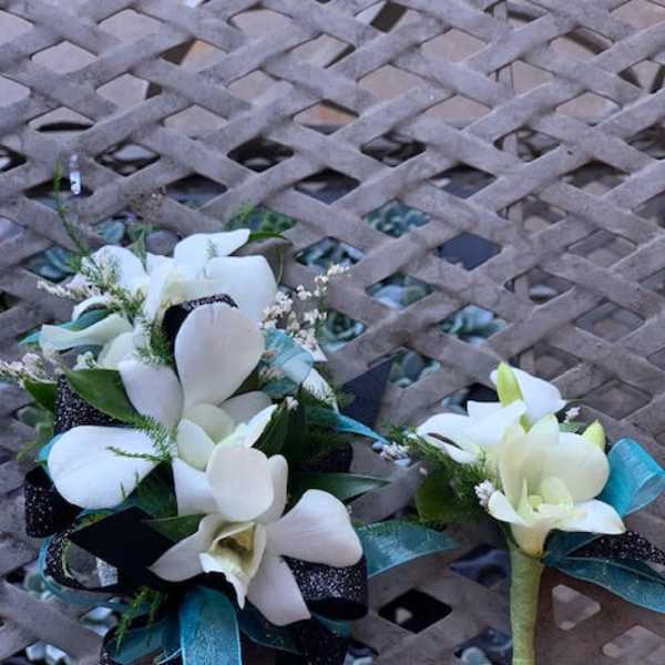 Two white floral corsages with teal ribbon accents on a lattice table