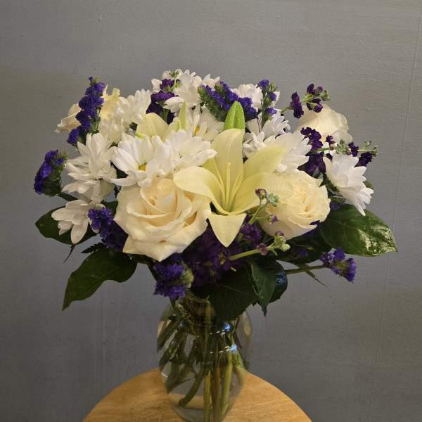 Bouquet of white daisies, cream roses, and purple filler flowers in a glass vase