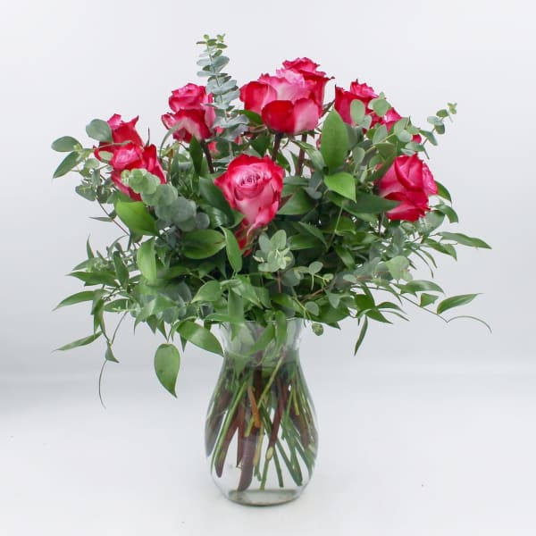 Pink roses arranged in a clear glass vase with greenery
