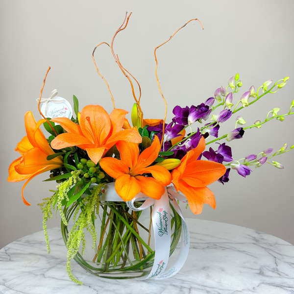 Orange lilies and purple orchids in a glass vase with ribbon