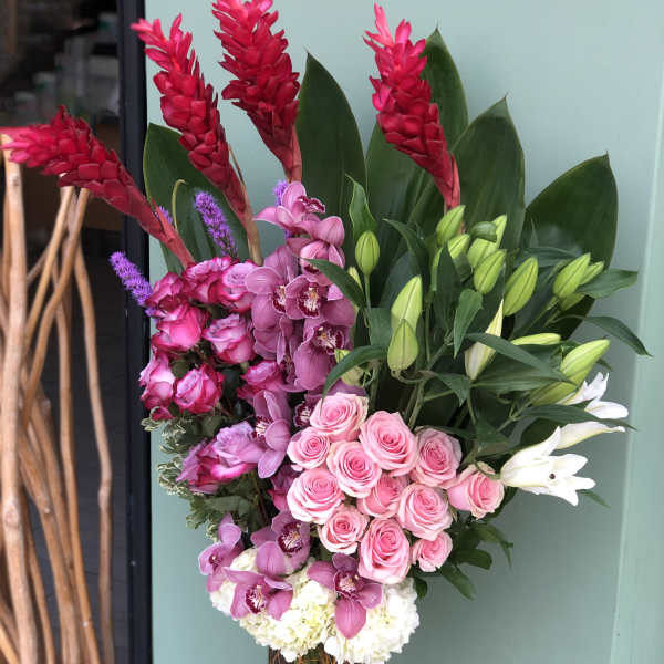 Tall bouquet of pink roses, orchids, lilies, and red tropical blooms in a glass vase.
