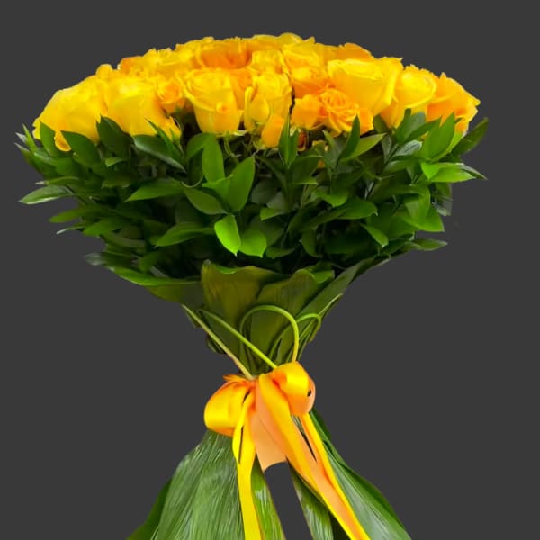 Bouquet of yellow roses wrapped with green leaves and a yellow ribbon