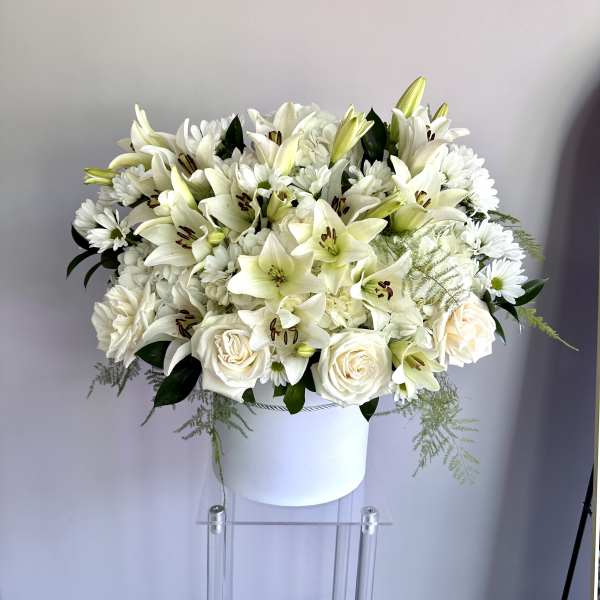 Round arrangement of white lilies, roses, and mums in a white hatbox-style container