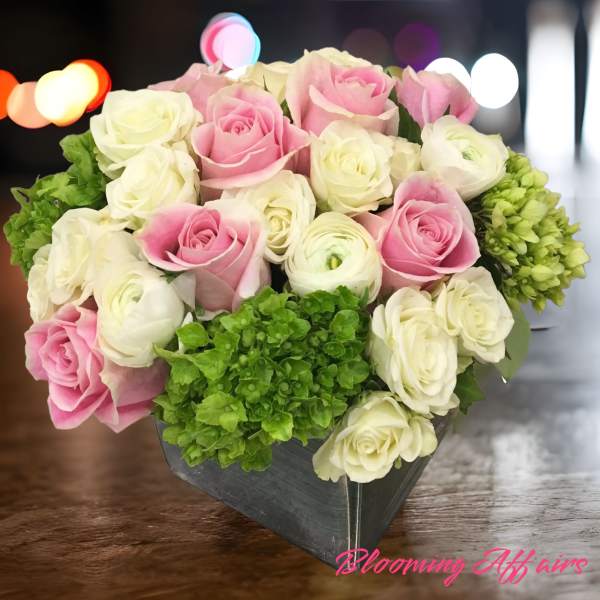 Pink and white roses arranged in a black box with green hydrangeas