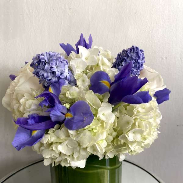 White hydrangeas and purple irises arranged in a green glass vase
