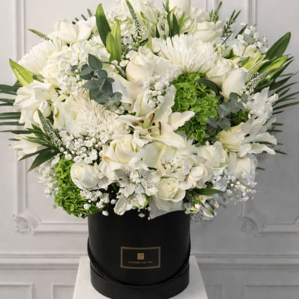 White floral arrangement in a black hat box with green accents