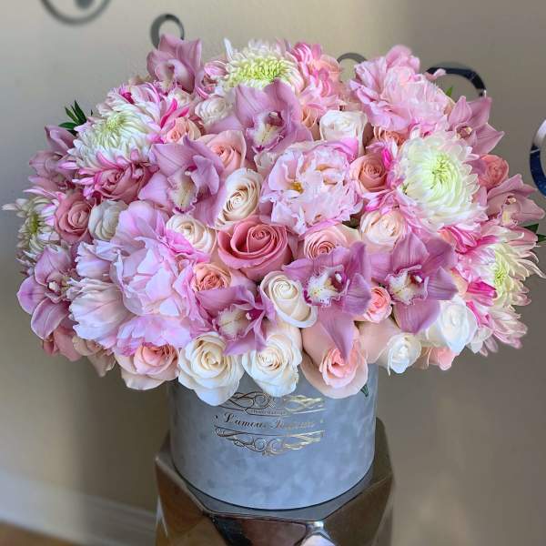 Lush hatbox arrangement of pink and white roses, peonies, orchids, and chrysanthemums in a round gray box