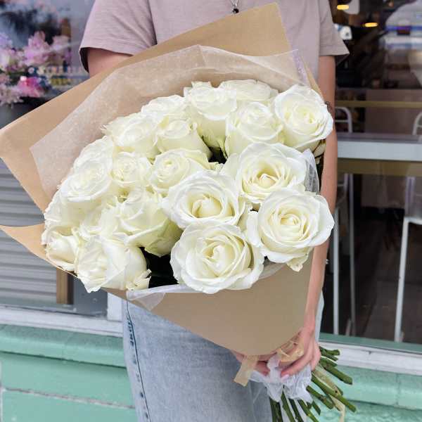 Large bouquet of white roses wrapped in kraft paper, held by a person outside a shop