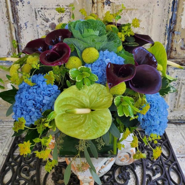 Colorful arrangement with blue hydrangeas, dark calla lilies, and green anthurium