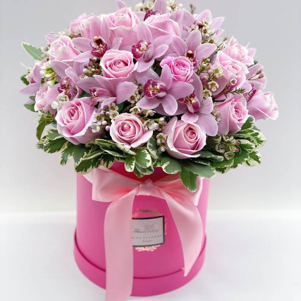 Pink roses and orchids arranged in a round pink box with a ribbon