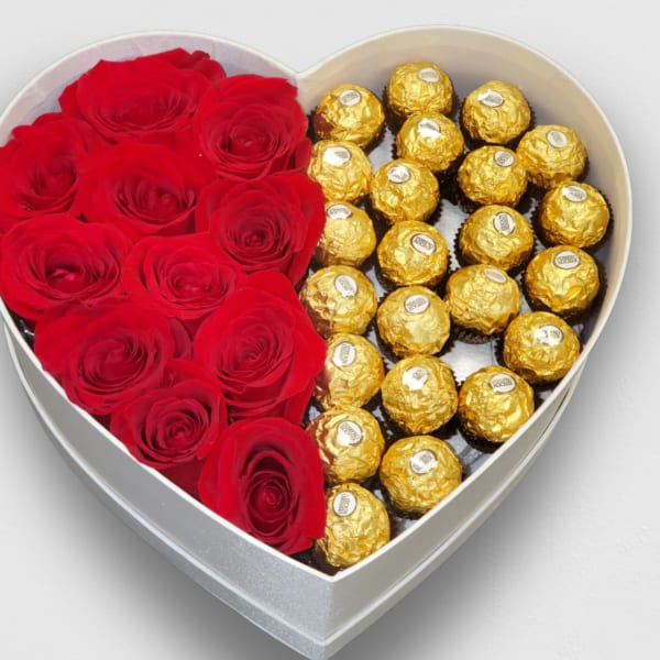 Heart-shaped white box half filled with red roses and half with gold-wrapped chocolates