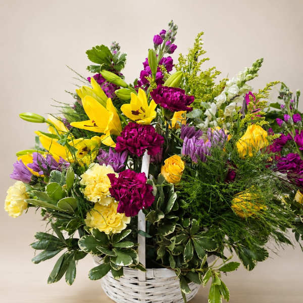 Basket arrangement of yellow lilies, purple flowers, and pink carnations