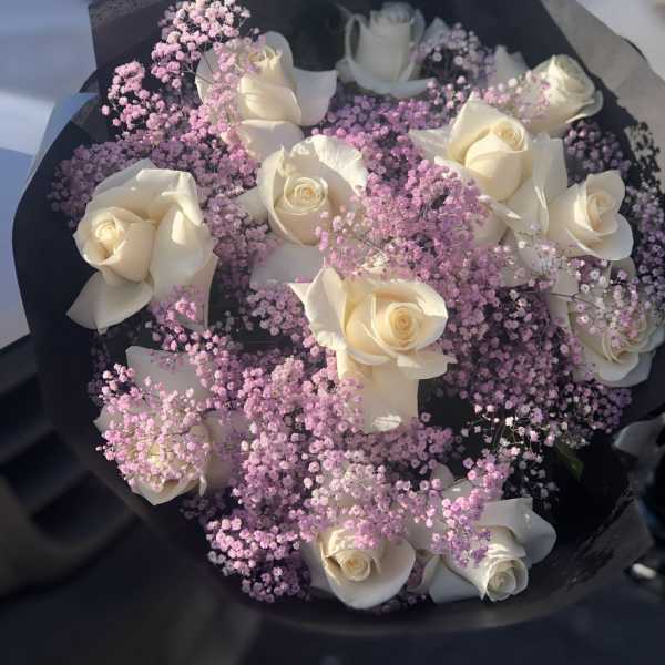 Bouquet of white roses with pink baby's breath in black wrap