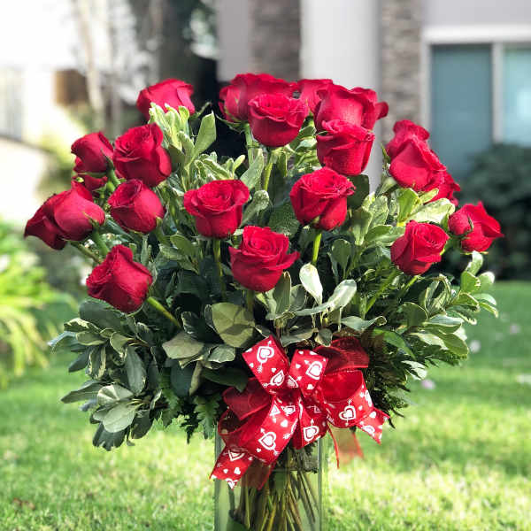 Bouquet of red roses in a tall glass vase with a red heart ribbon