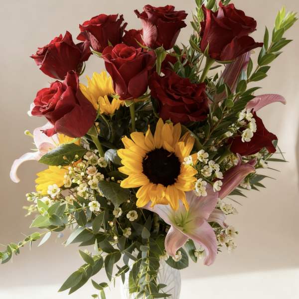 Bouquet of red roses, sunflowers, and pink lilies in a clear vase