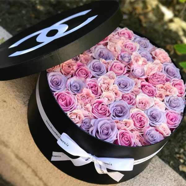 Round box filled with pink and lavender roses, tied with a white ribbon