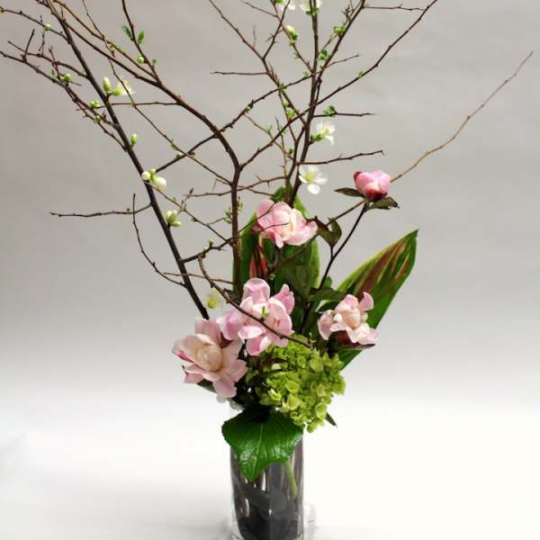 Tall floral arrangement with pink blossoms and branching twigs in a glass vase