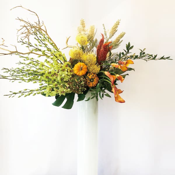 Tall autumn floral arrangement in a white vase with orange and yellow blooms