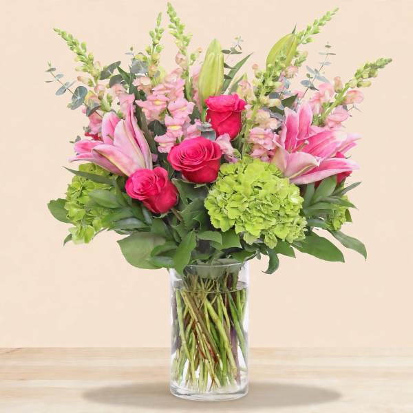 Pink lilies and roses with green hydrangea in a clear glass vase